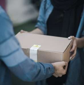 Close-up image of a delivery person handing a parcel box to a customer
