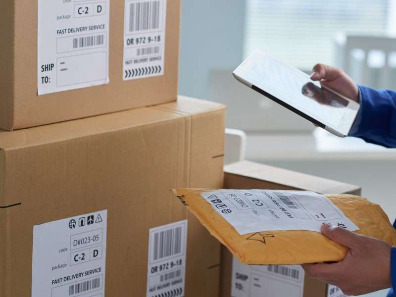 Freight delivery person checking labels on packaging with tablet